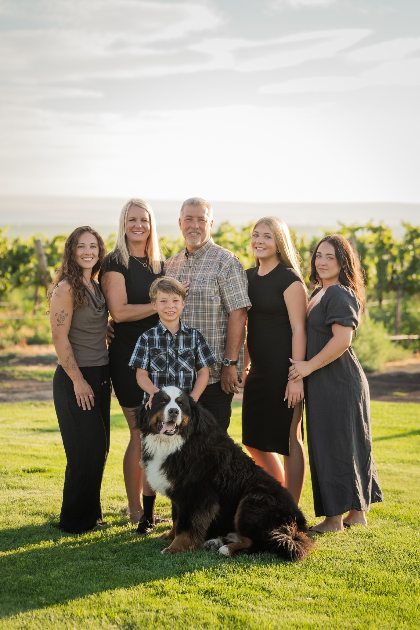 A family of six posing with their dog in warm vineyard light.