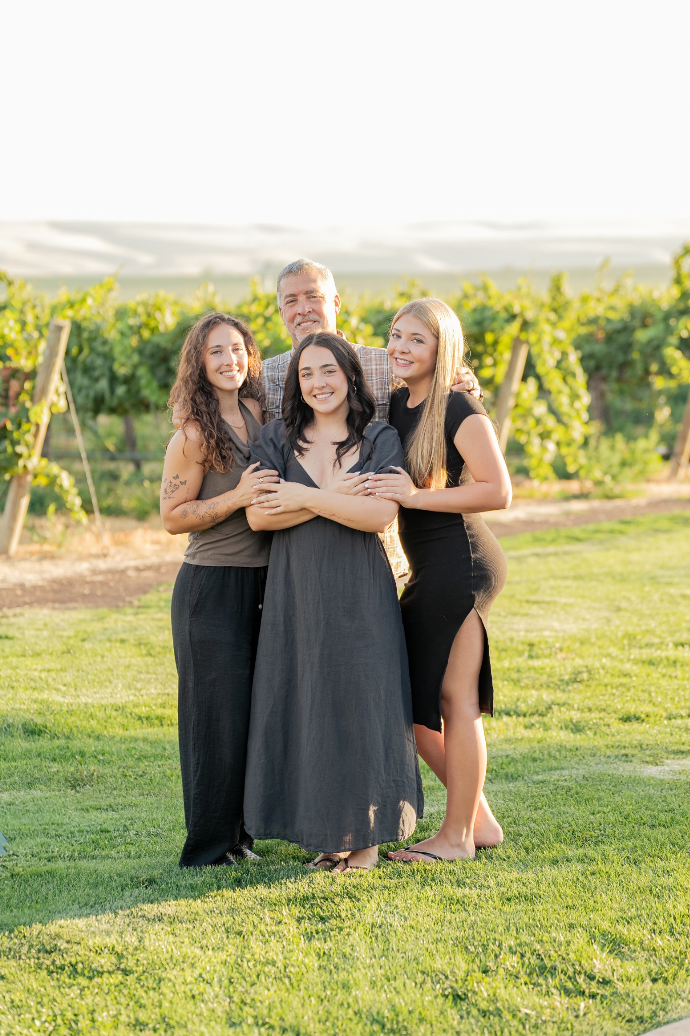 Three sisters embracing in a vineyard at sunset.