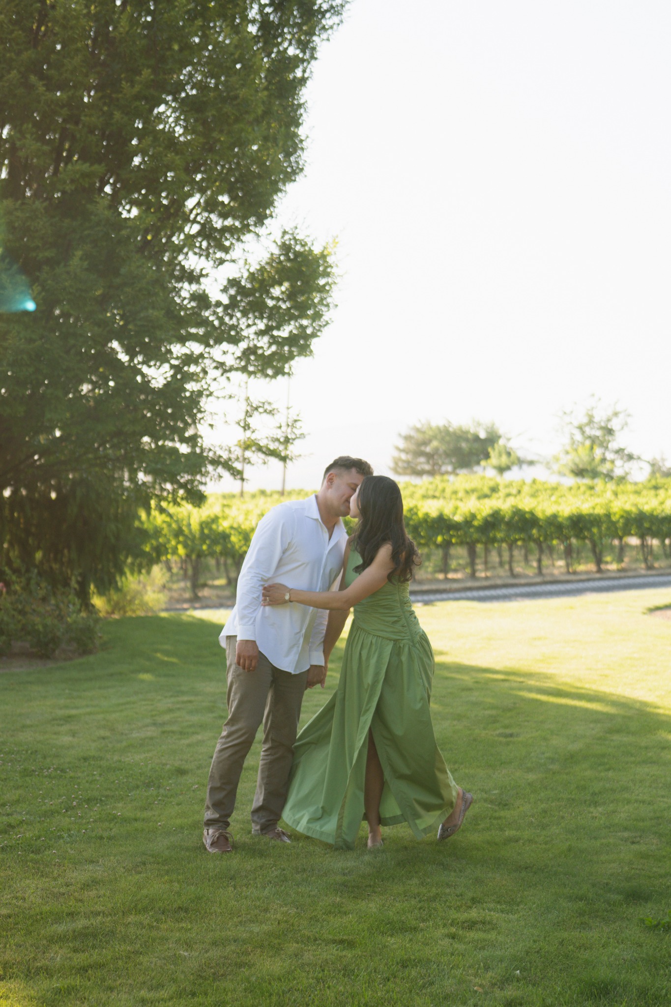 A couple kissing in soft evening light beside a vineyard.