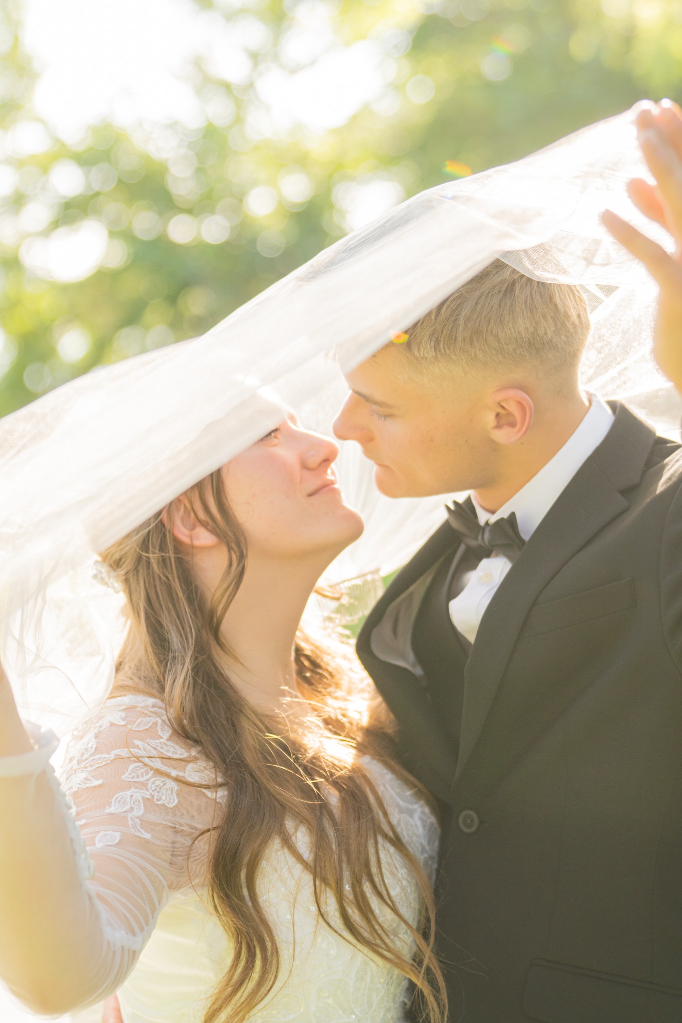 A bride and groom sharing a kiss beneath her veil in glowing sunlight.
